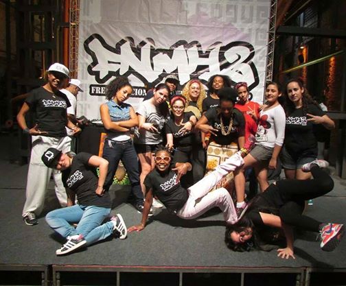 Grupo de dançarinas e dançarinos posa diante do painel do Festival FNMH2